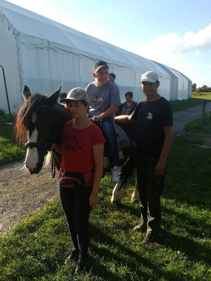 Grupa ludzi pozuje na zewnątrz w pobliżu namiotu; jedna osoba siedzi na czarno-białym koniu, podczas gdy inni stoją obok niej.